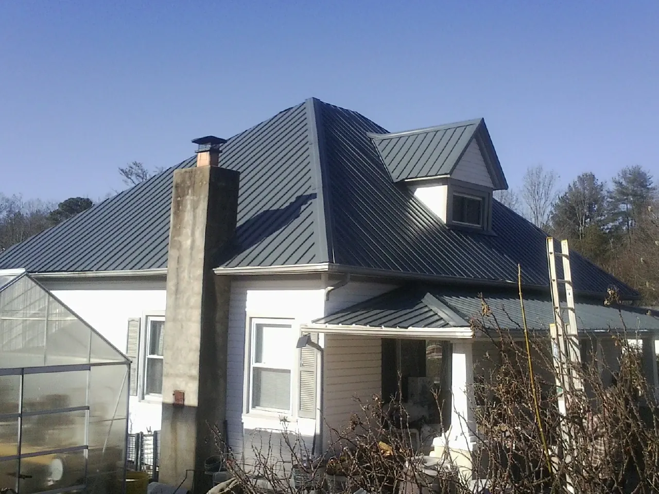 Dark blue standing seam metal roof on a white farmhouse with dormer — Slate & Tile Roof Repair by Roofing Brothers in Maskell