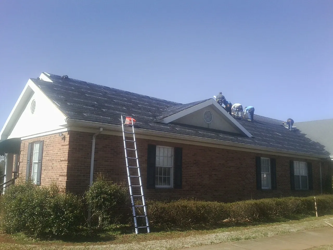 Crew tearing shingles off a brick ranch roof with a ladder set — Emergency Roof Repair work by our crew in Maskell