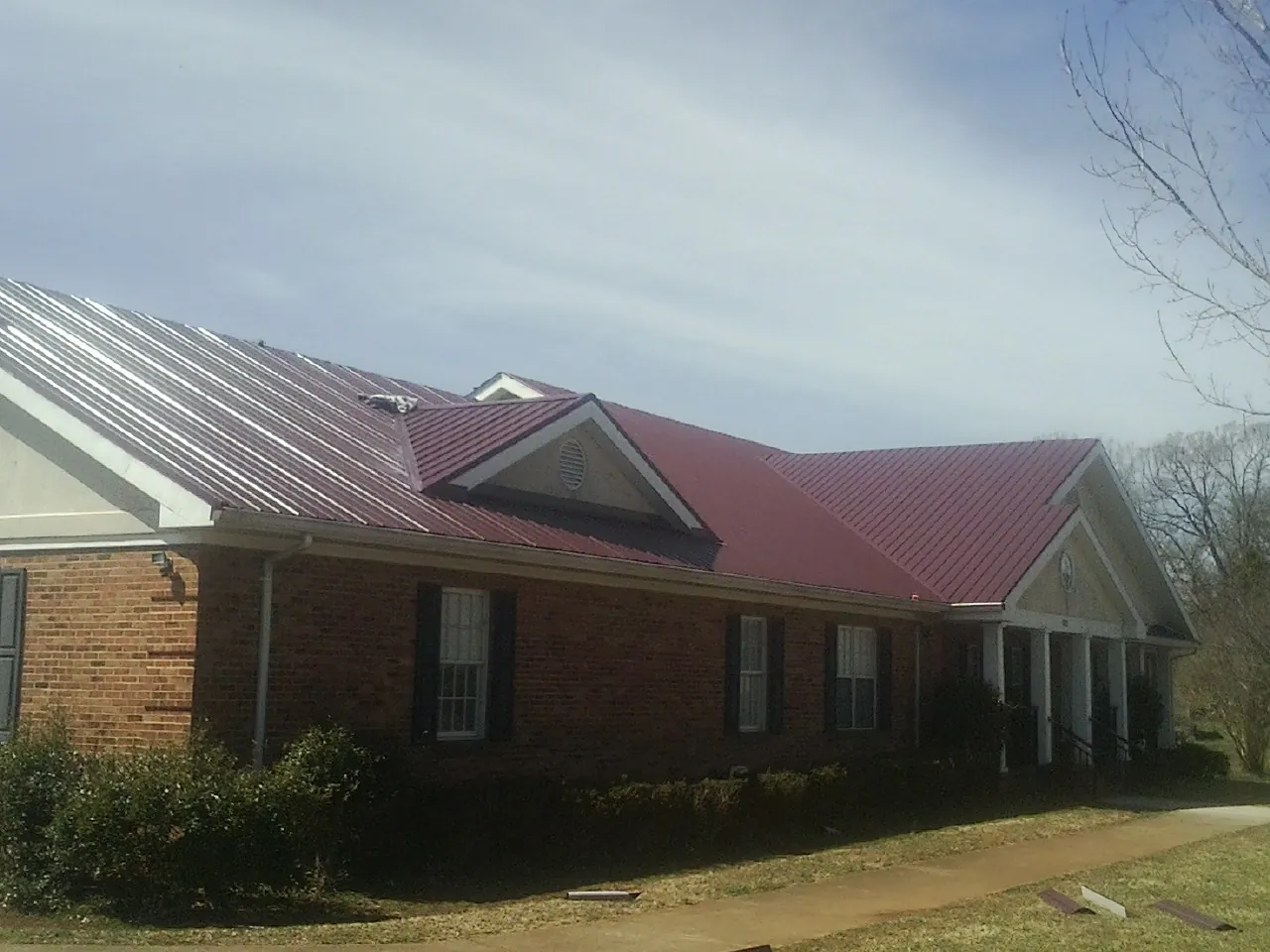 Red metal roof with gabled entries on a long brick building, from a Hail Damage Roof Repair job in Maskell