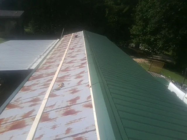 Old rusted panels beside newly installed green metal roofing — Wind Damage Roof Repair by Roofing Brothers in Maskell