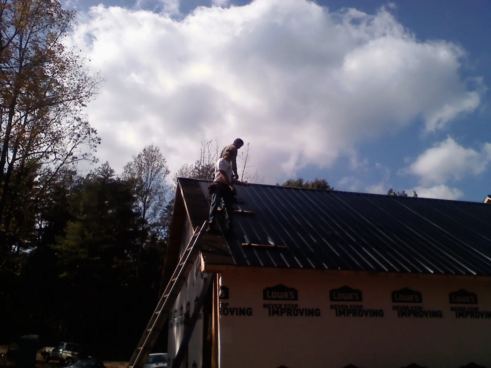 Roofer fastening dark metal panels high against a cloudy sky, from a Roof Inspection job in Maskell